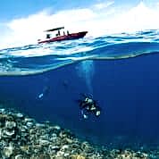Scuba diver underneath small red motor boat investigating coral.