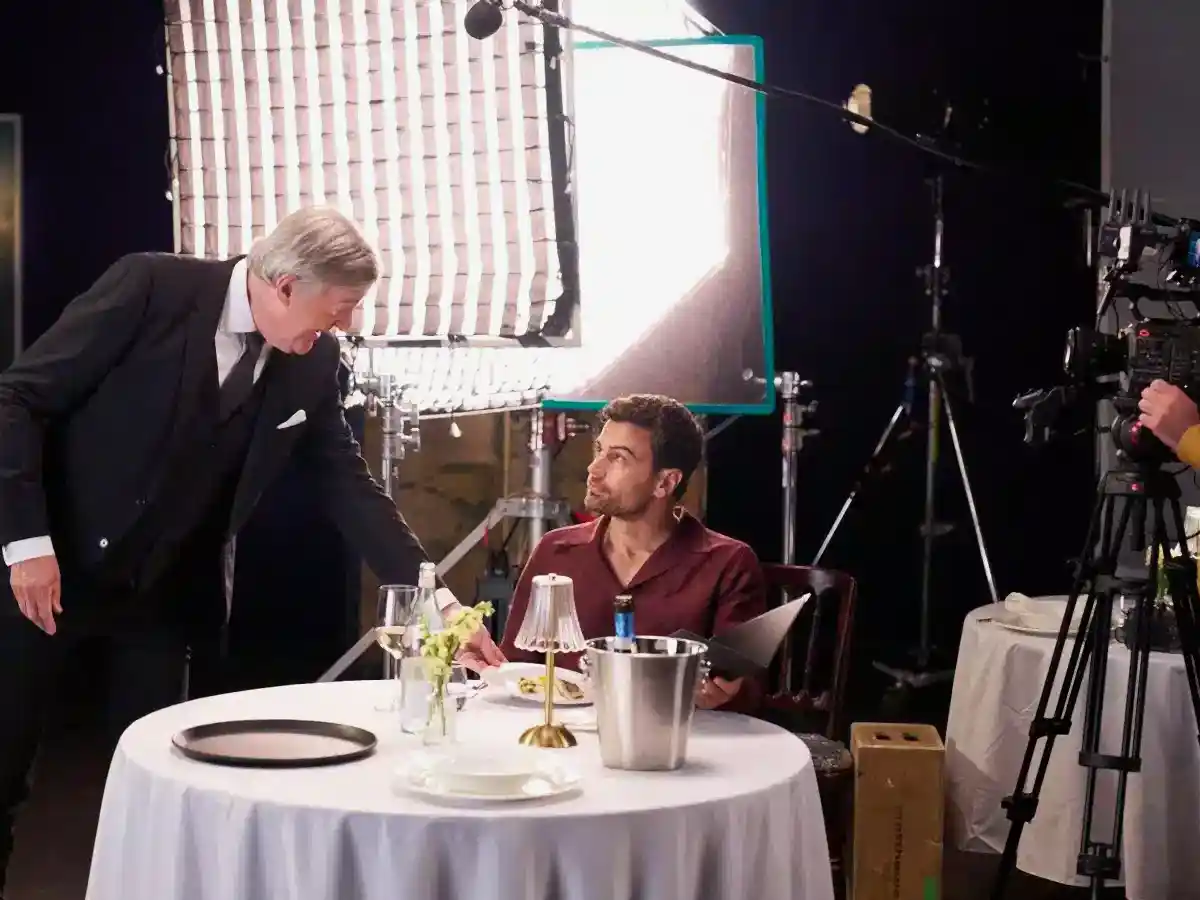 Stephen Fry serving a plate to Theo James seated at a table